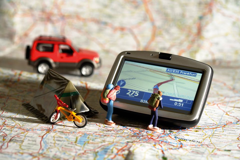 Игрушечные люди, палатка, велосипед и машина на карте рядом с GPS-навигатором
